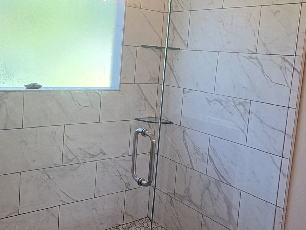 A walk-in shower with marble-look tile and clear glass after a deep clean